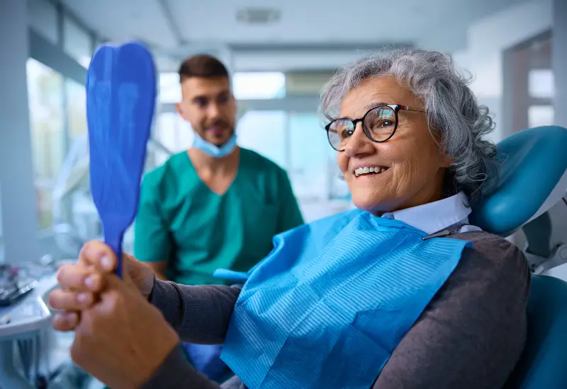 A female patient looks in the mirror at her teeth in her dentist’s Parker, CO office