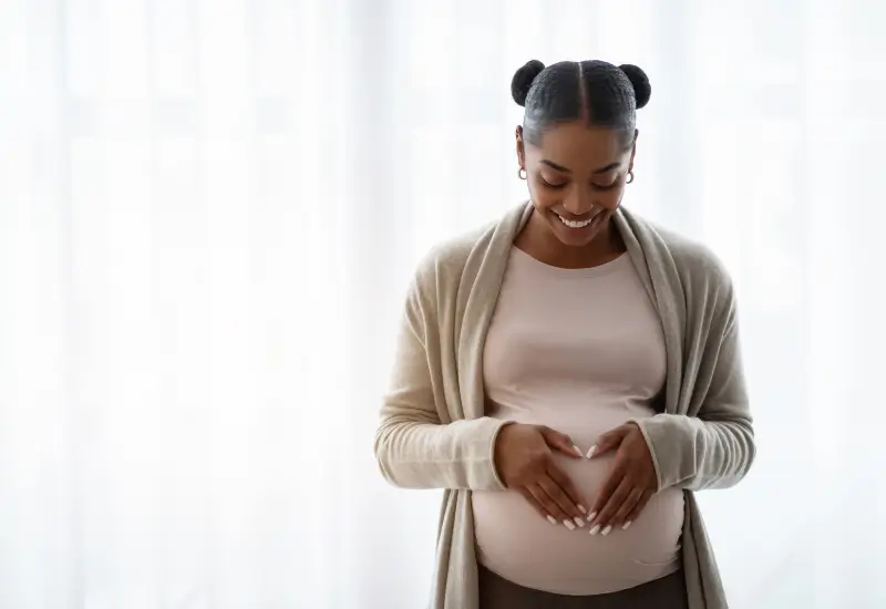 A pregnant woman with a beautiful smile holds her belly in Parker, CO