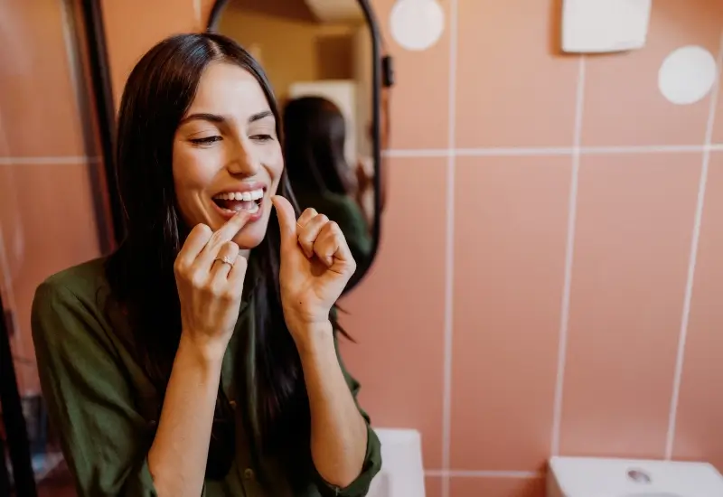 A woman practices oral hygiene by flossing her teeth twice daily in Parker, CO