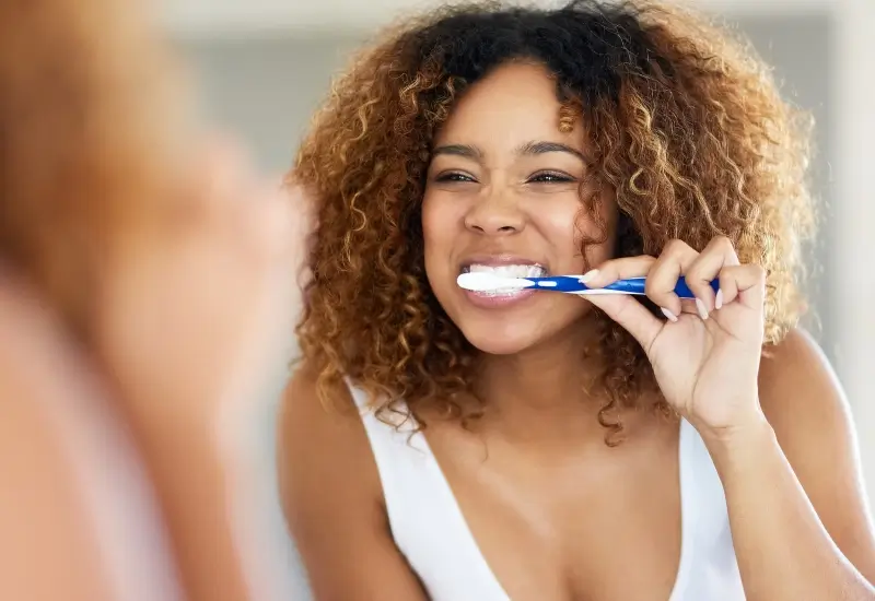 A woman looks in the mirror as she brushes her teeth to prevent tooth decay in Parker, CO